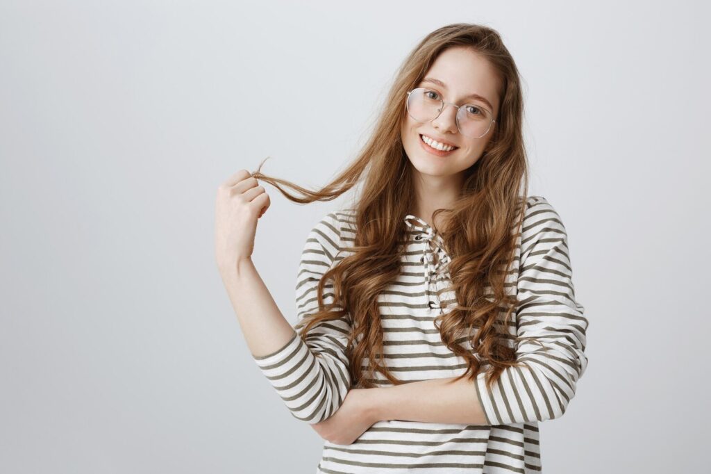 A Smiling Woman Holding Her Long Wavy Hair, Representing The Confidence Gained After A Personalized Hair Loss Plan New York.
