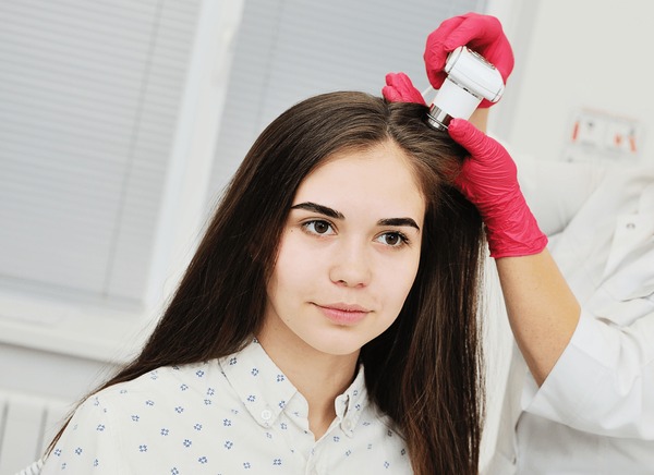A Young Woman Receiving A Trichology Scalp Care And Scalp Detox New York Assessment Using A Handheld Diagnostic Tool To Check For Scalp Health And Buildup.
